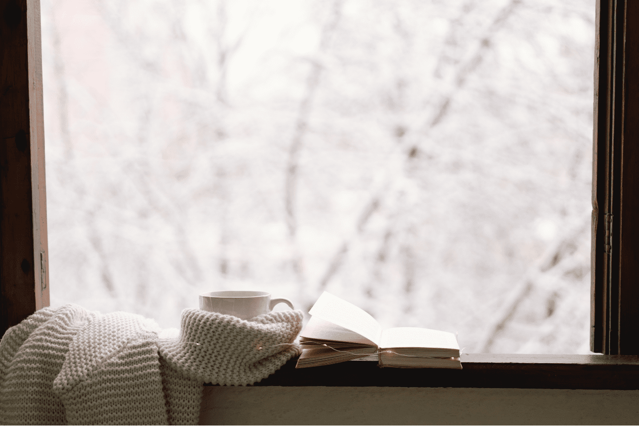 Book, mug, and sweater on windowsill overlooking winter scene