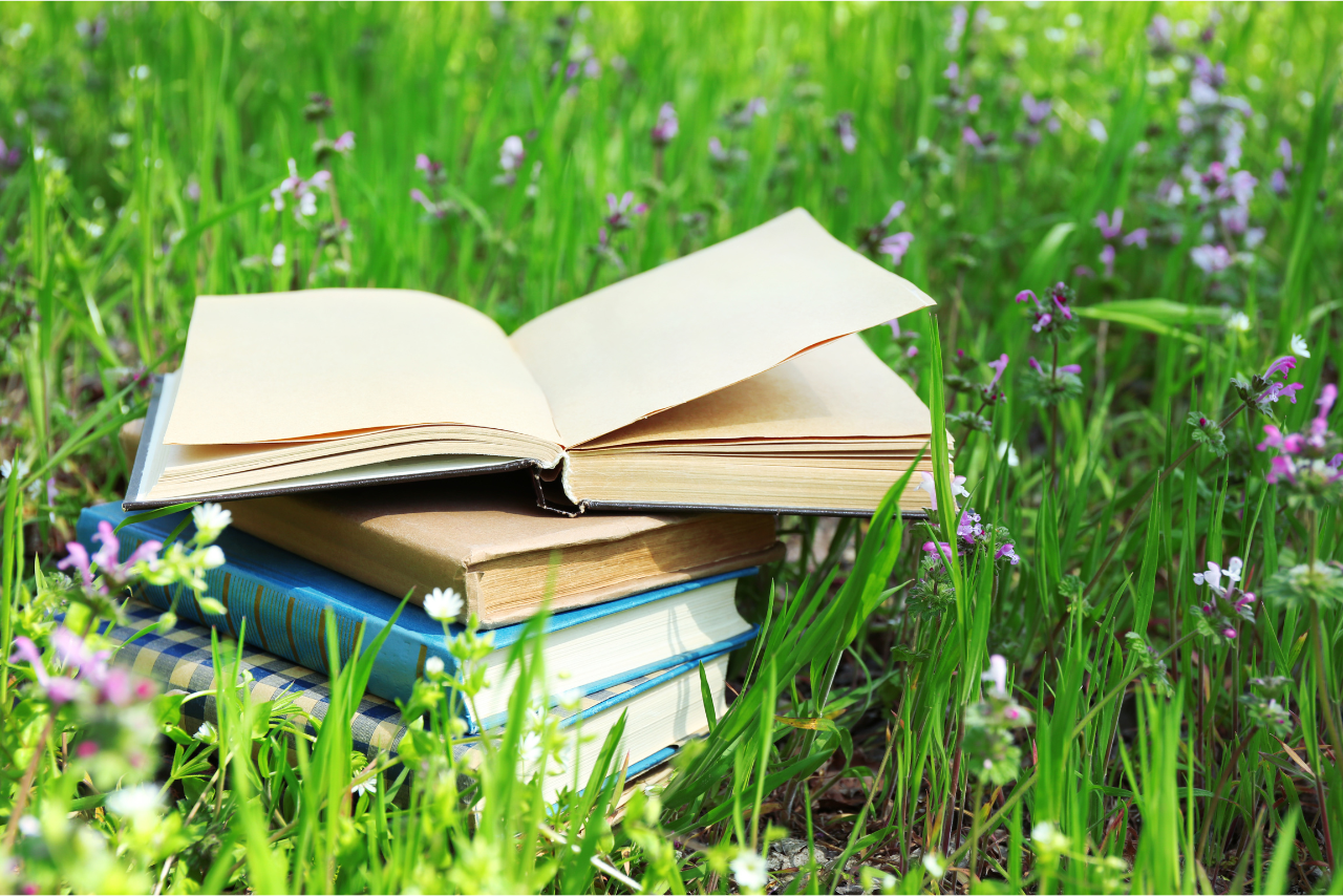 stack of books in field with spring flowers