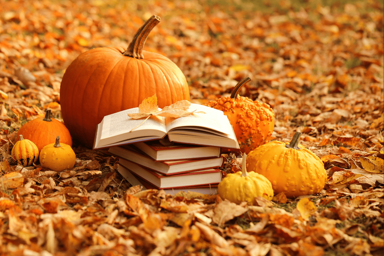 stack of books on fall leaves with pumpkins around them